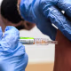 Gloved hands administer a flu shot to someone's arm