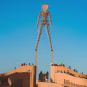 A large wooden man sculpture, The Man, stands in Black Rock Desert, Nevada, surrounded by festival participants in colorful costumes and bicycles