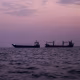 Three commercial vessels floating in the water at sunset.