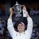 Elena Rybakina holds a silver trophy in the air with both hands.