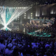 A wide view of the audience, judges, and a performer on stage during American Idol.