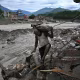 A man carrying a bag as he walks past a damaged house.