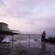 A couple observing a purple sunset over a cloudy sky on the Hawaiian coastline.