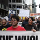 Protestors holding a large white banner reading THE WHOLE SYSTEM IS GUILTY!