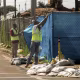 Workers in yellow vests removing blue tarp from a chainlink fence.