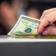 A hand resting on a counter top holds a 20 dollar bill