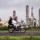 Image: Two men on a motorbike ride past an oil refinery in Jamnagar.