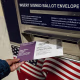 The hand of a person inserting a mail ballot into a drop box.