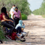 Families and small children from Central America and Mexico sit in a field near the Rio Grande river after being apprehended by U.S. Border Patrol agents on on May 25, 2021.