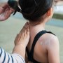Cropped Hands Of Woman Applying Suntan Lotion On Back Of Daughter At Poolside