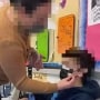 A teacher in the North Penn School District tapes a mask onto a student’s face.