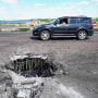 A car drives past a crater caused by a Ukrainian rocket strike on on Kherson's Antonovsky (Antonivskiy) bridge on July 21, 2022.