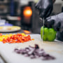 Chef in black latex gloves cutting vegetables in his kitchen in restaurant.