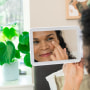 Woman putting lotion under her eye, while looking in the mirror