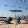 Two people sit in blue beach chairs on the sand of Gansevoort Peninsula beach, overlooking the Hudson River in Manhattan