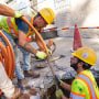 Construction employees in yellow vests work in sidewalk opening as they replace pipes