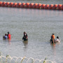 Image: Asylum-seeking migrants walk in the Rio Grande river between the floating fence 