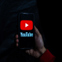 A person holds a mobile phone with the YouTube logo on the screen.