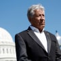 Mario Andretti listens during a news conference with the Capitol seen in the background