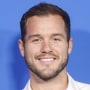 Neck up of Colton Underwood smiling in front of a light blue background