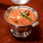 A dish of butter chicken is presented on a dining table in a silver chalice