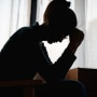 Silhouette photo of young woman sitting alone in bedroom with face in hands