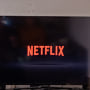 A couple sits in front of a television with the Netflix logo on it.