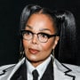 Janet Jackson looks ahead wearing glasses and a white blazer