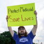 Two people hold signs outside, one the left it says "Medicaid funds critical disability services", and on the right it says "Protect Medicaid, Save lives"