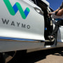 A passenger steps into a Waymo minivan parked outside