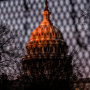 The U.S. Capitol dome as seen behind a fence with barbed wire, as the sun rises, the sky is purple