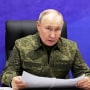 Russian President Vladimir Putin sat holding a papers against a purple background