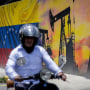A motorcycle rider passes in front of an oil-themed mural.