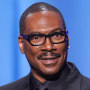 Eddie Murphy holds a trophy with a chrome star on the top while standing on stage