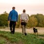 Rear view of couple with dog walking on field at sunset
