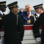 Donald Trump and Pete Hegseth saluting behind a coffin being carried by service members in formal uniforms.
