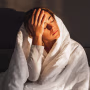 Woman has a headache and sitting in bed covered with blanket.
