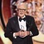 John Lithgow holding an Emmy, dressed in a tuxedo.