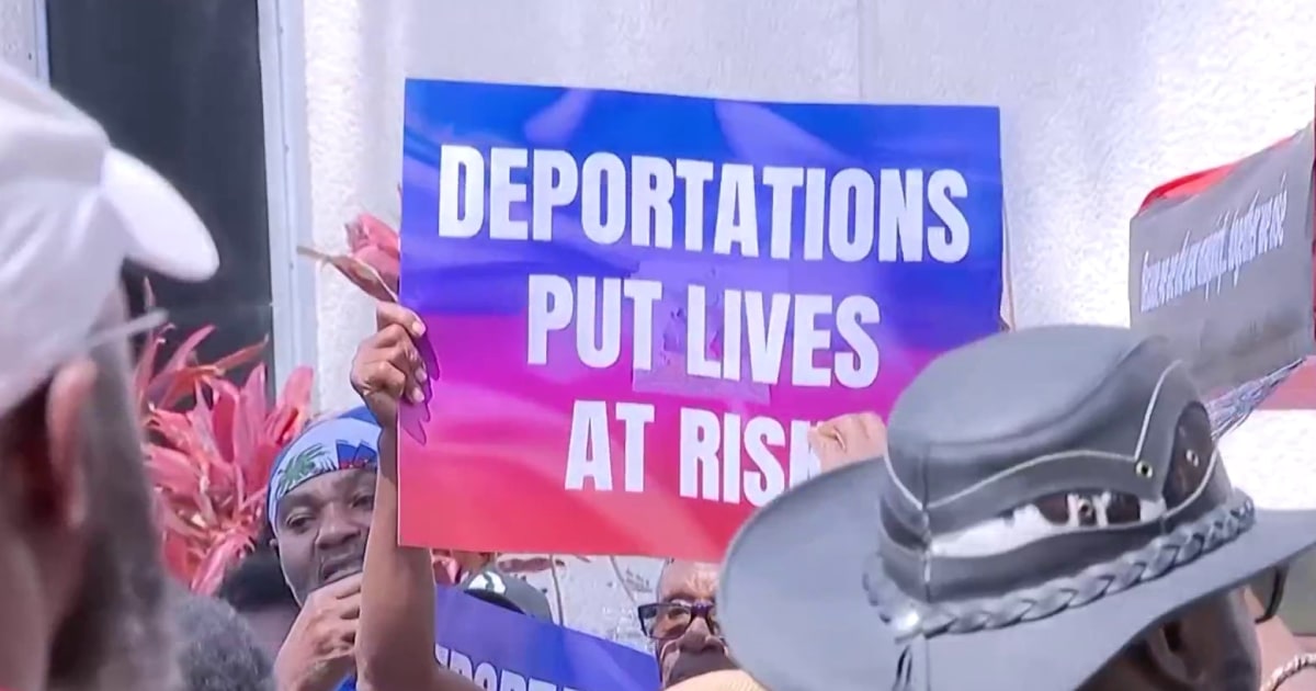 A person holds a protest sign reading 'DEPORTATIONS PUT LIVES AT RISK' amidst a crowd.
