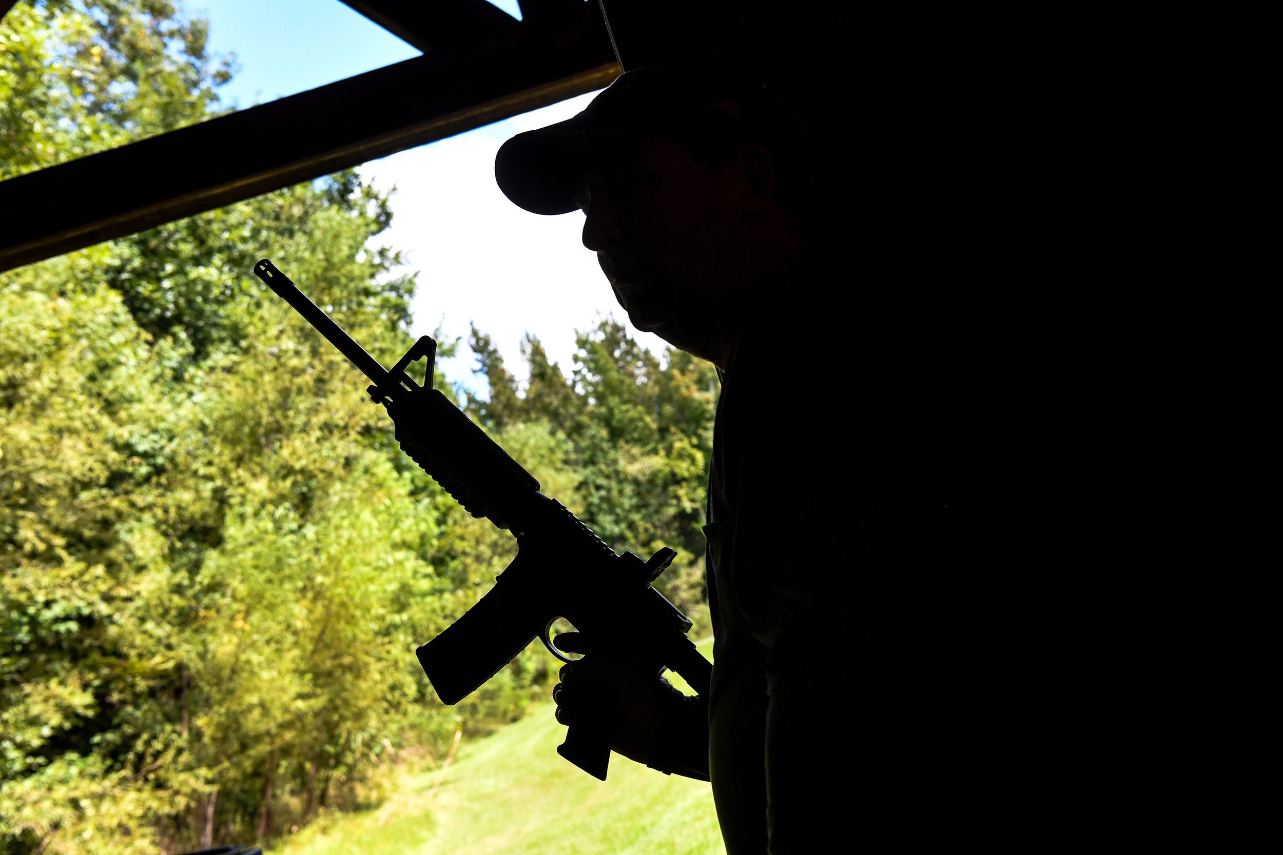 Photo of a silhouetted man in a ball cap holding up an AR-15